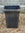 Dark wooden planter box on a gravel surface with a stone wall background