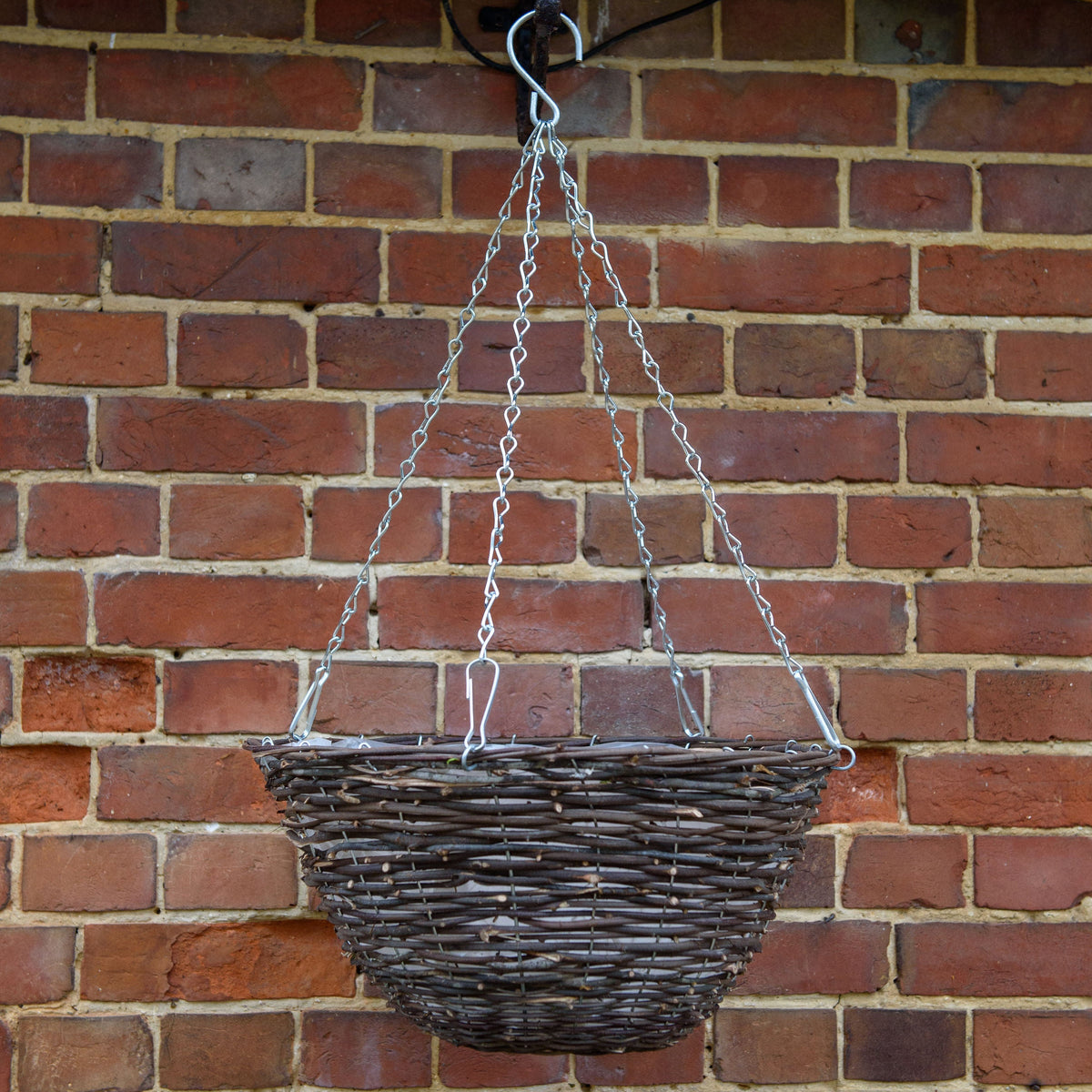 Wicker hanging basket on a chain against a brick wall