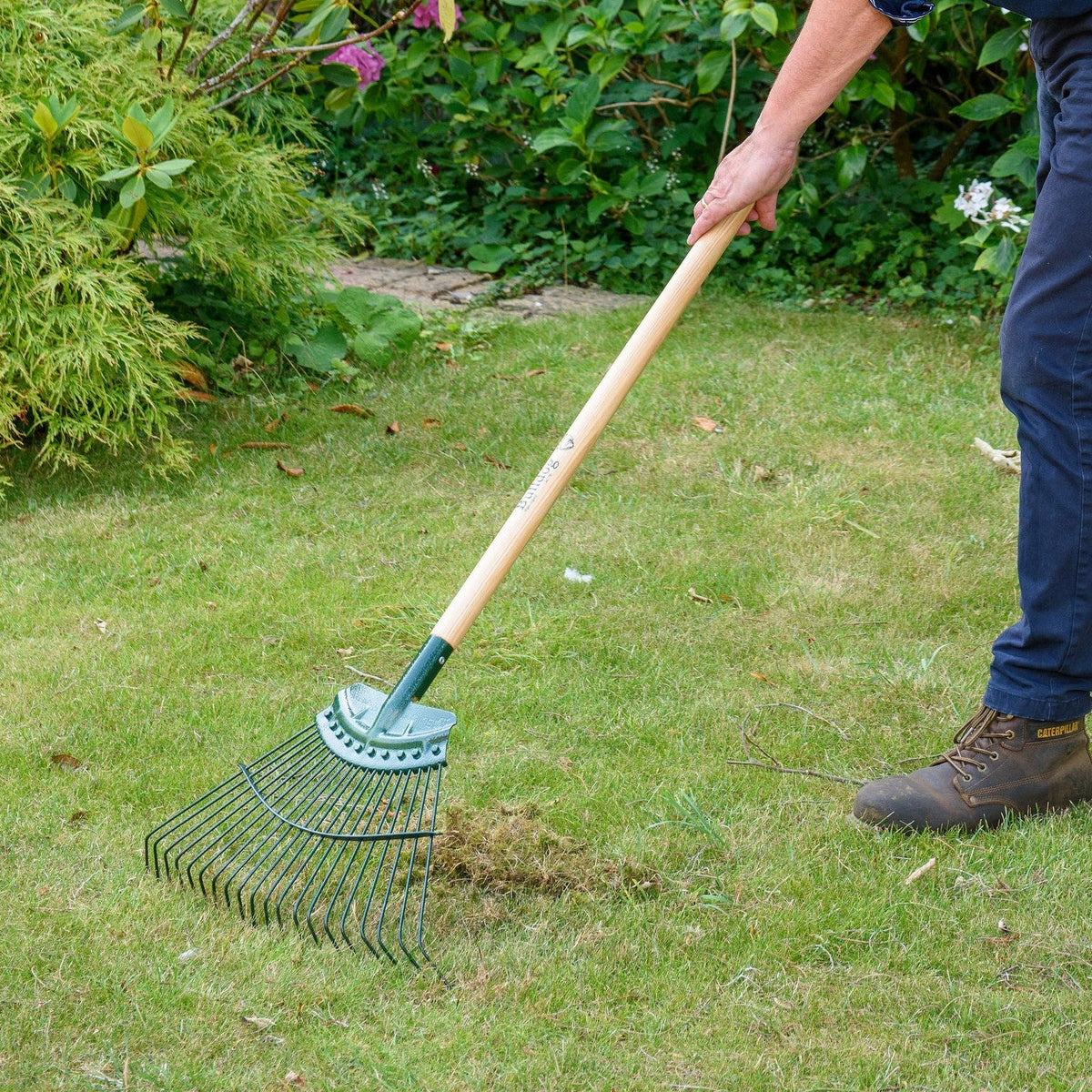 Person using a Bulldog Springbok garden rake on a grassy area with plants in the background