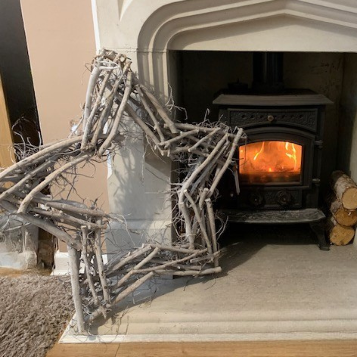 Wooden star wreath sculpture in front of a lit wood stove.