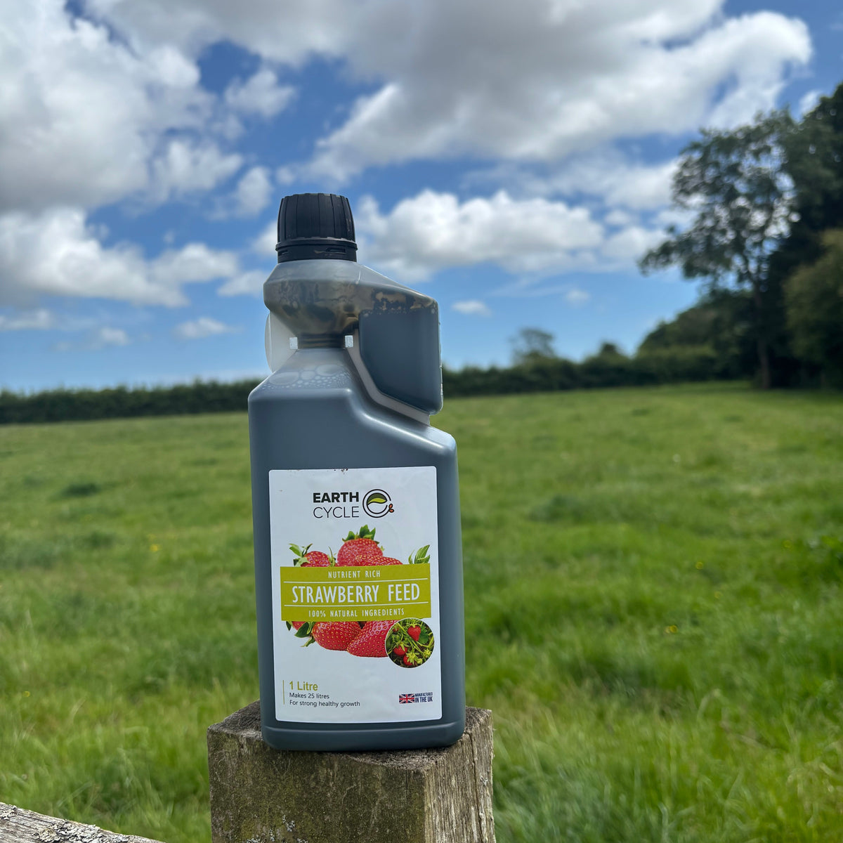Bottle of Earth Cycles Tomato Feed against a natural background with grass and blue sky.