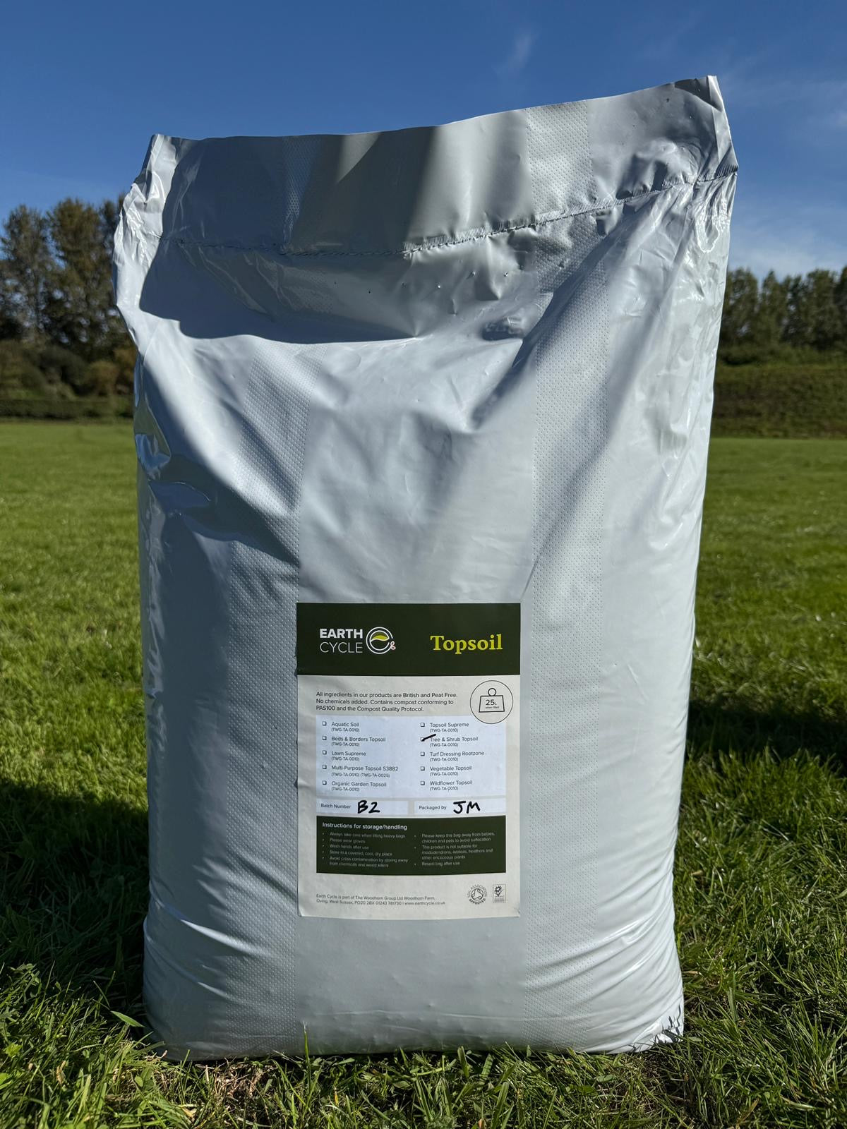 Bag of topsoil labeled 'Earth Choice' on a grassy field with trees in the background.