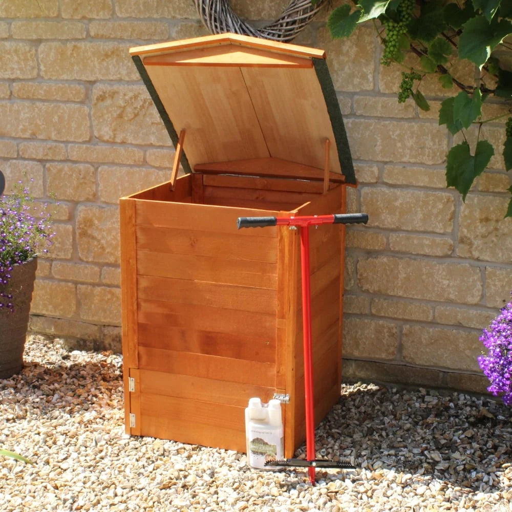 Wooden compost bin with a red compost trowel against a stone wall.