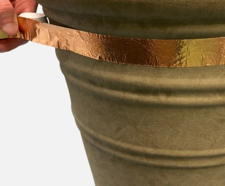 Person applying gold leaf strip to a green metal bucket