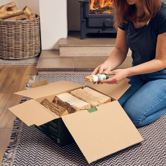 Person unpacking a box of firewood and holding firelighters in front of a fireplace.