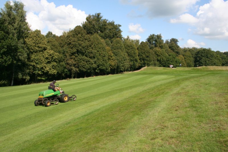 A green lawn with a green and yellow lawn mower parked on it, surrounded by freshly cut grass.